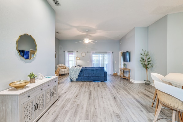 A spacious living room with a blue sofa, a dining area with a white table, and a ceiling fan. - Heart of Lake County! Family Escape w/ Lanai, Pool (Tavares)