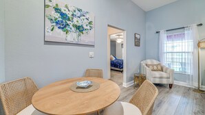 Un comedor con una mesa redonda de madera, sillas de mimbre, un cuadro en la pared y vistas a otra habitación.