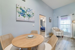 A dining area with a round wooden table, wicker chairs, a painting on the wall, and a view into another room. - Heart of Lake County! Family Escape w/ Lanai, Pool (Tavares)