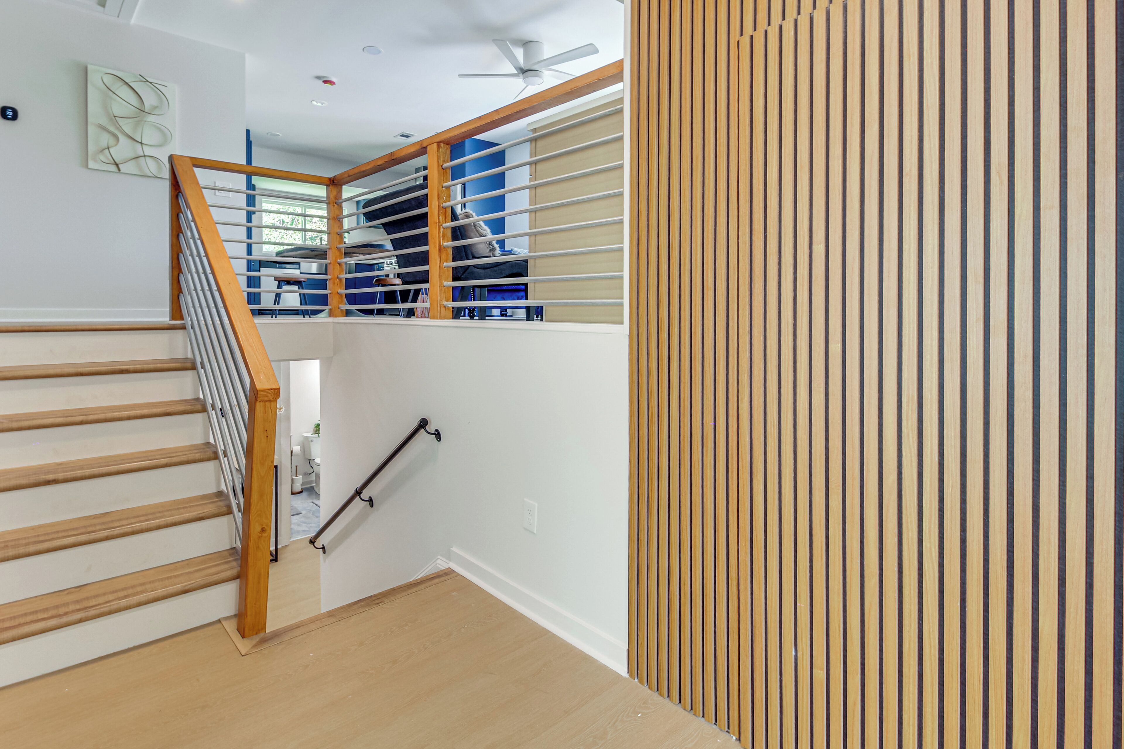 A modern staircase with wooden steps and metal railings, leading to a room with a blue wall and a ceiling fan.