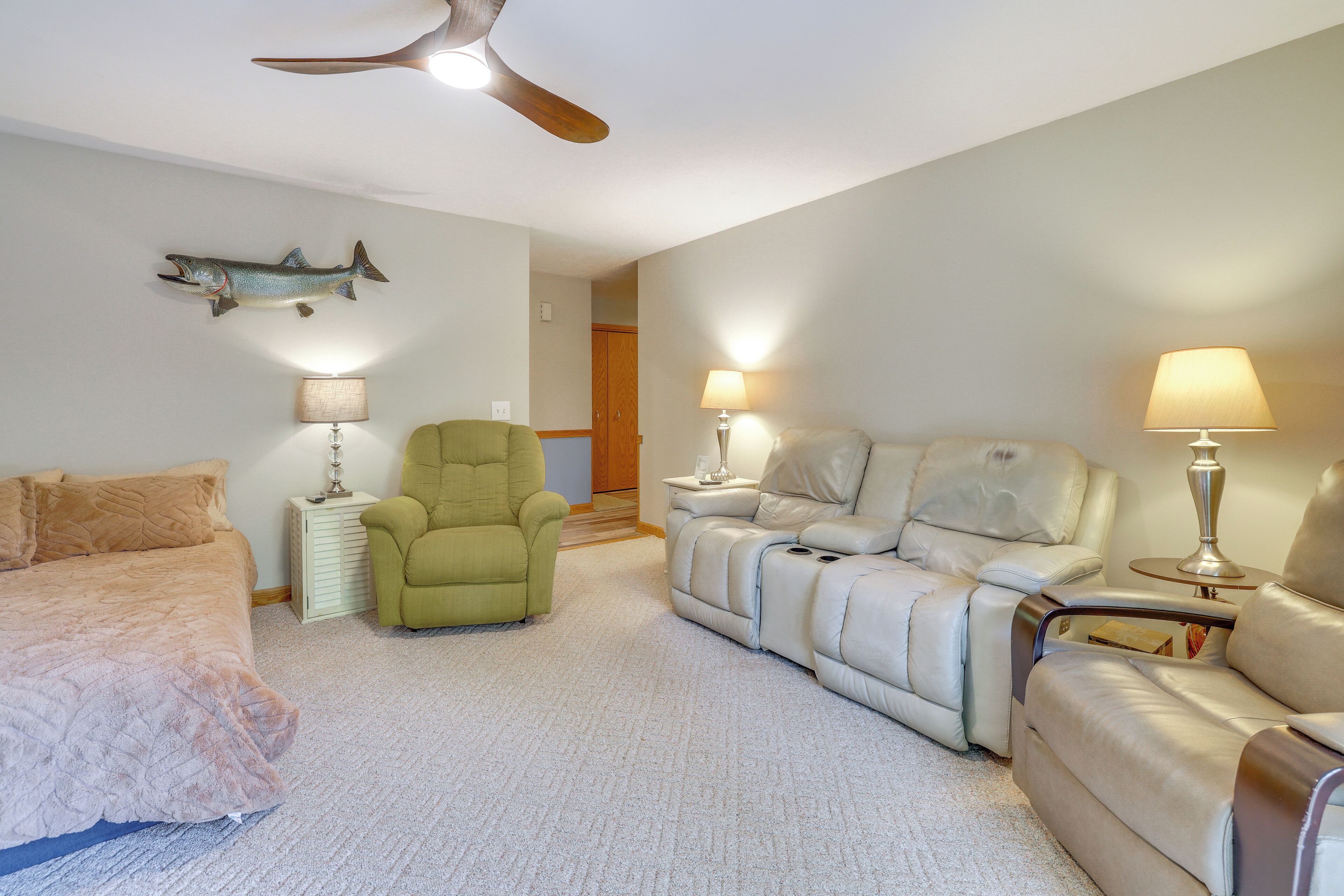 A bedroom with a bed, a green armchair, a leather sofa, two lamps, a ceiling fan, and a fish wall decoration.