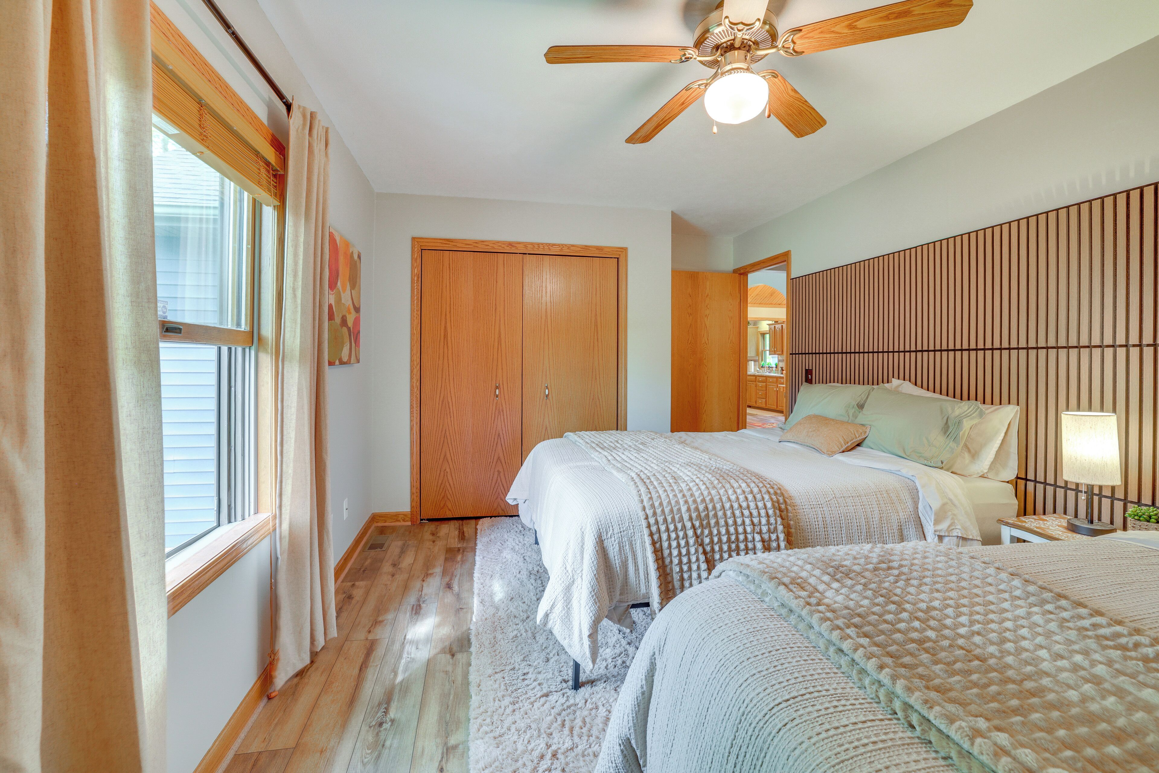 A bedroom with two beds, a ceiling fan, a wooden wardrobe, and a window with curtains.