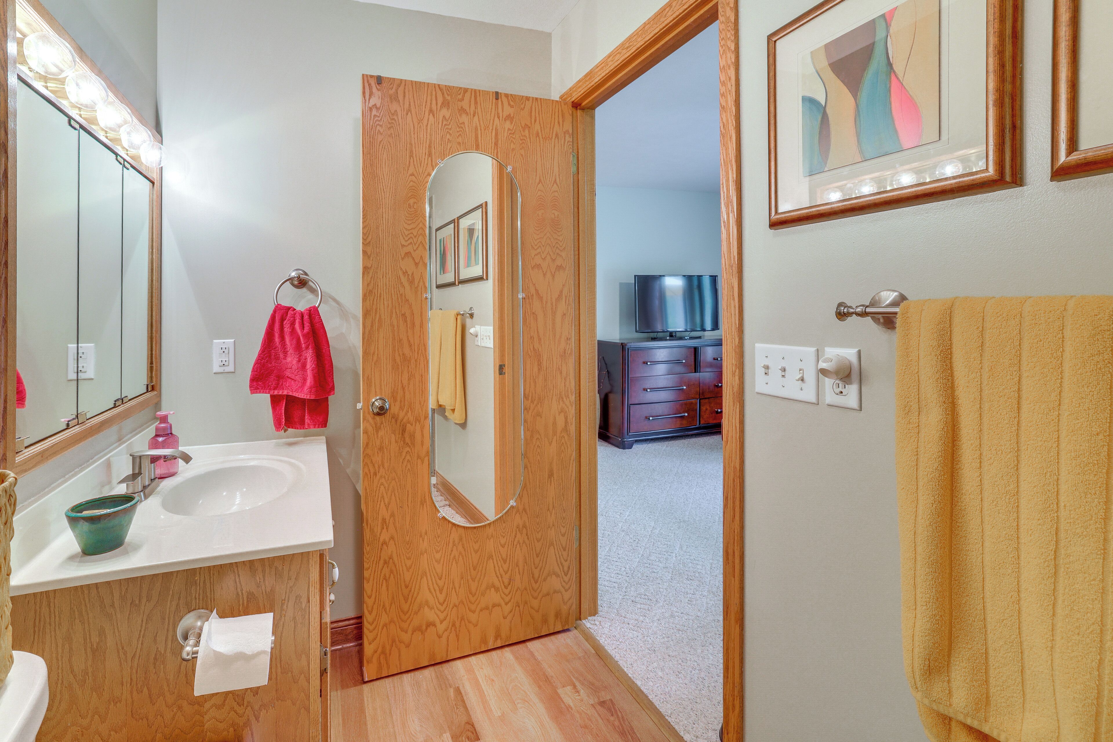 A bathroom with a wooden door, a sink, a mirror, and a towel rack.