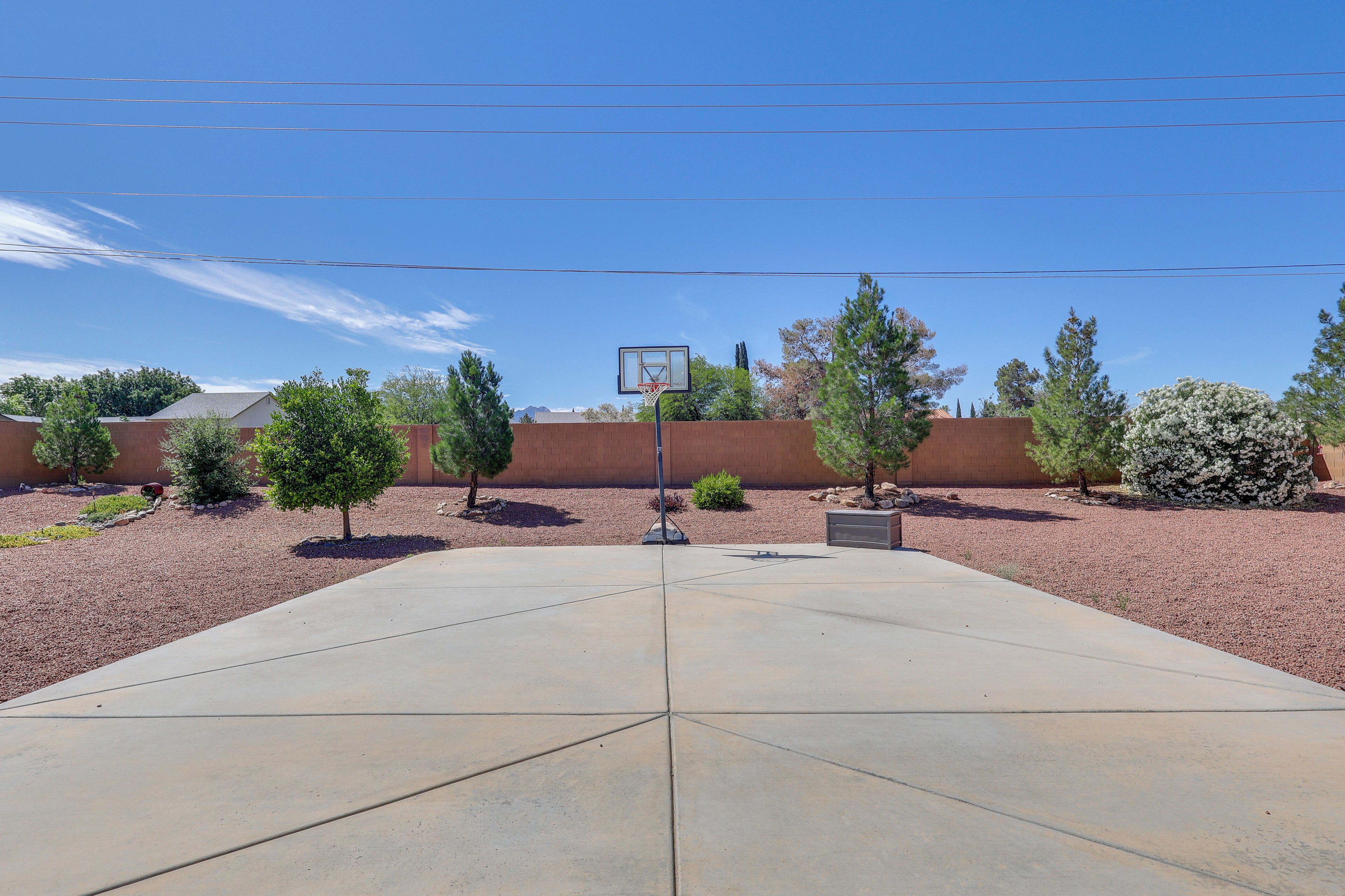 A basketball court with a hoop, surrounded by a landscaped area with trees and shrubs.