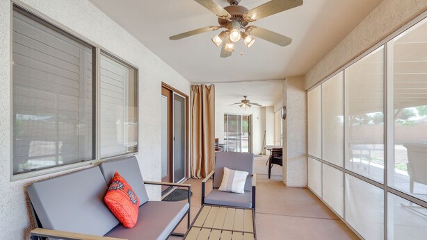 Un espacio al aire libre cubierto con ventilador de techo, un banco acolchado, una silla y una mesa.