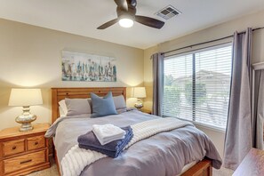 Ein Schlafzimmer mit einem Bett, zwei Nachttischlampen, einem Deckenventilator, einem Fenster mit Jalousien und einem Bild an der Wand.