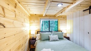 Une chambre dans une cabane en bois, avec un lit, des oreillers, une fenêtre et une table de chevet.