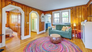 A room with wooden walls, a green sofa, a round ottoman, and a colorful rug. - 1/2 Mi to Lake & Dtwn! Elk Rapids 'cozy Cottage' (Elk Rapids)