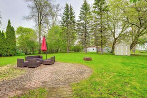 Eine runde Terrasse aus Ziegelsteinen mit Gartenmöbeln, umgeben von Rasen und Bäumen.