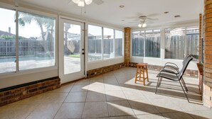 Eine geräumige Terrasse mit Deckenventilator, großen Fenstern und einer Ziegelwand.