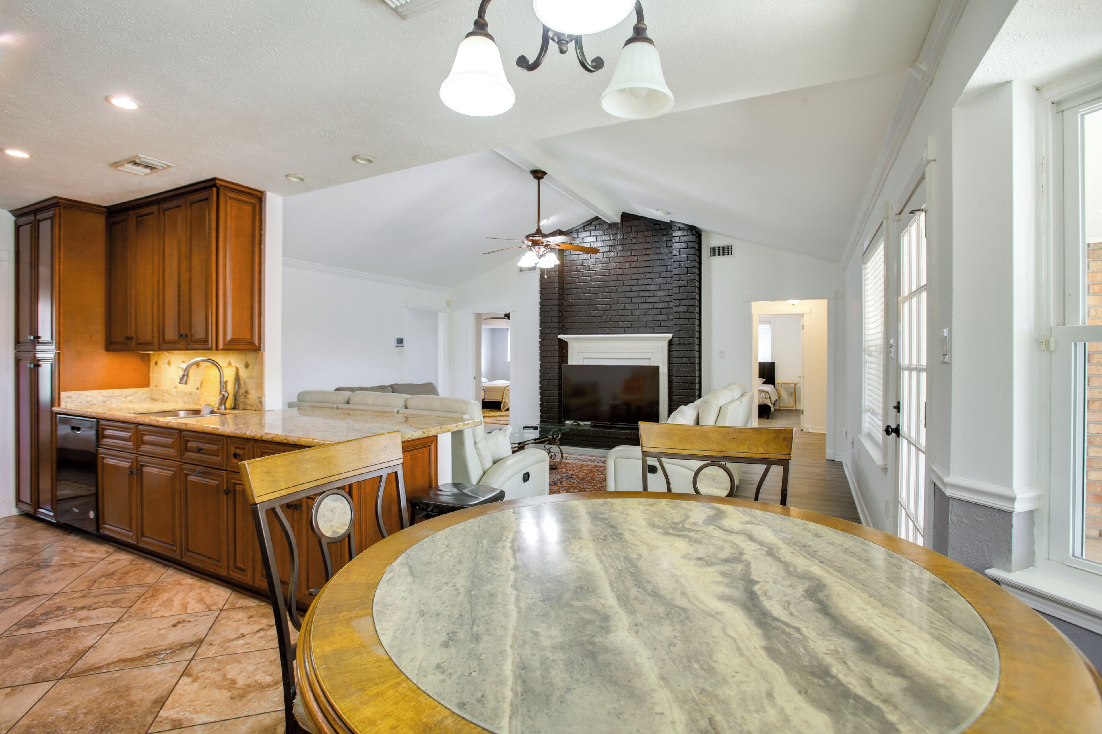 A spacious kitchen with wooden cabinets, a marble island, and a dining area with a round table.