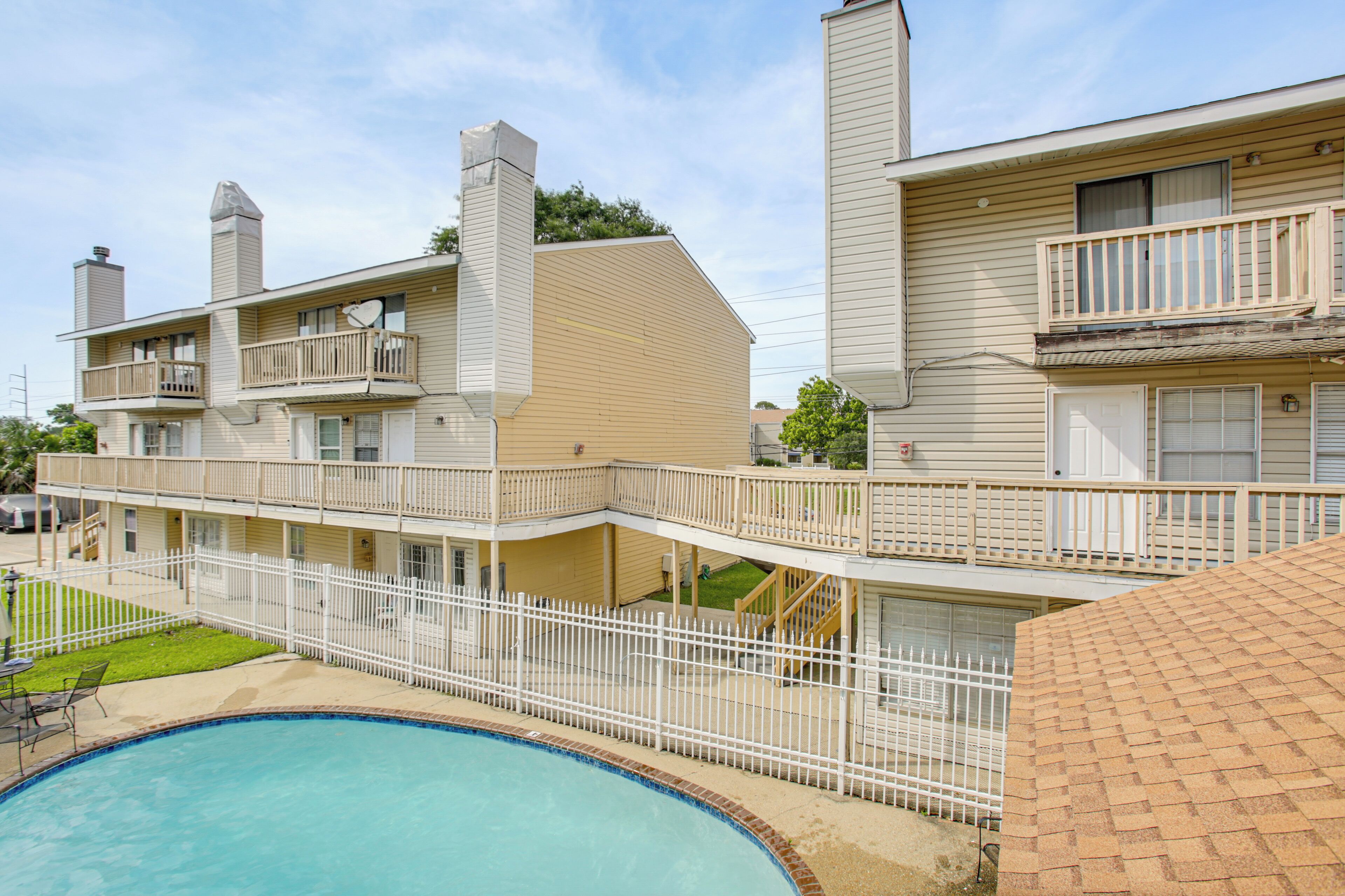 A two-story building with a swimming pool, balconies, and a fenced patio area.