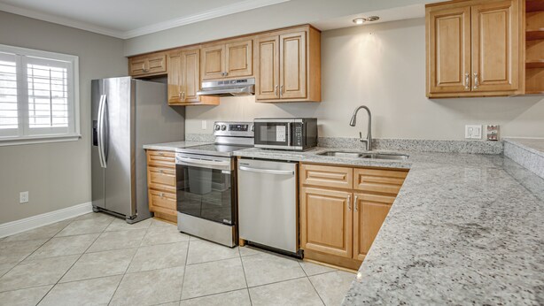 A kitchen with stainless steel appliances, wooden cabinets, a granite countertop, and a window with blinds. - Gateway to New Orleans! Modern Condo w/ Pool (Kenner)
