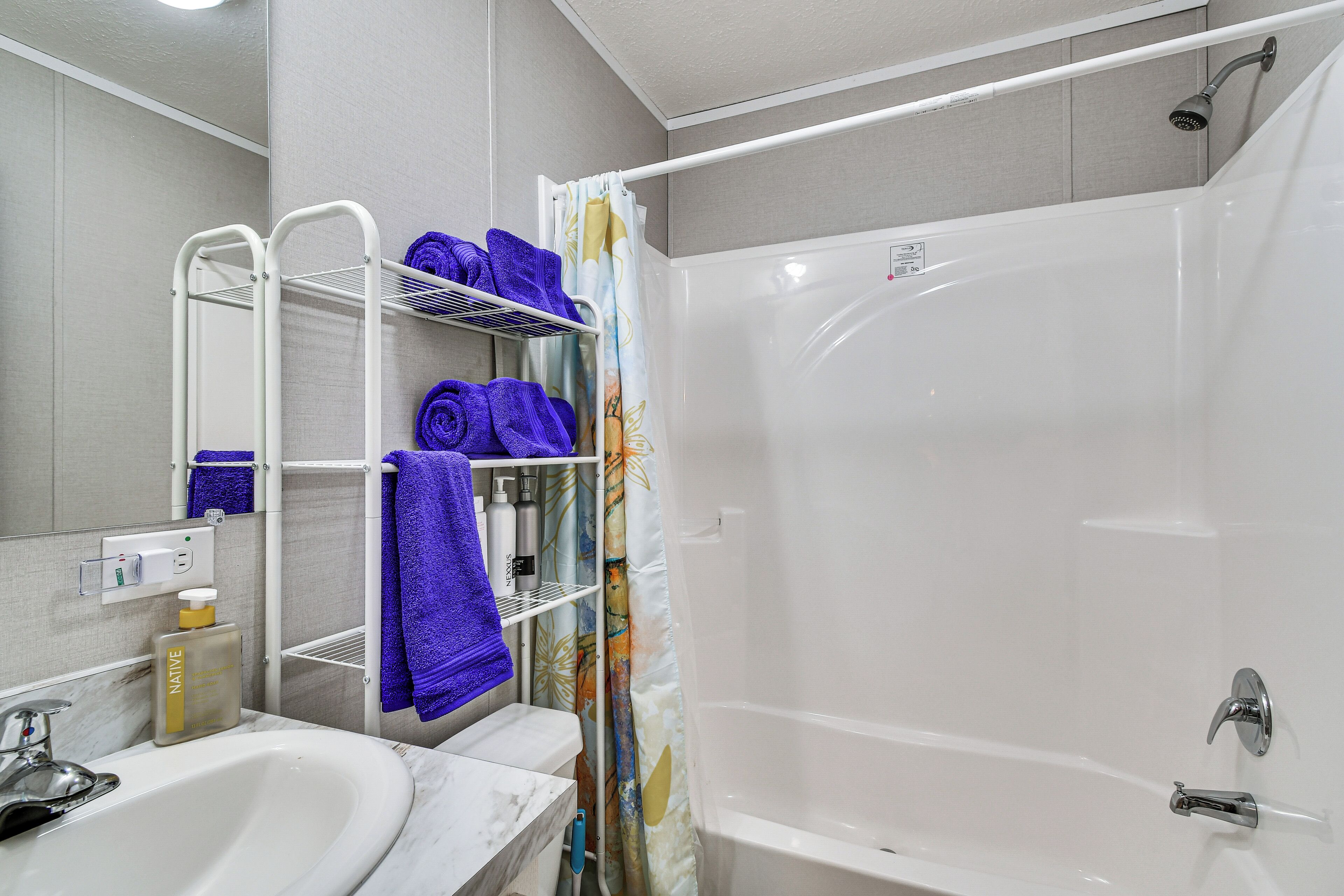 Een badkamer met een witte badkuip, een douche, een wastafel met een marmeren blad en een handdoekrek met blauwe handdoeken.