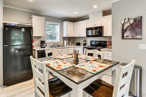 Una cocina moderna con armarios blancos, un refrigerador negro, electrodomésticos de acero inoxidable y una mesa de comedor con posavasos.