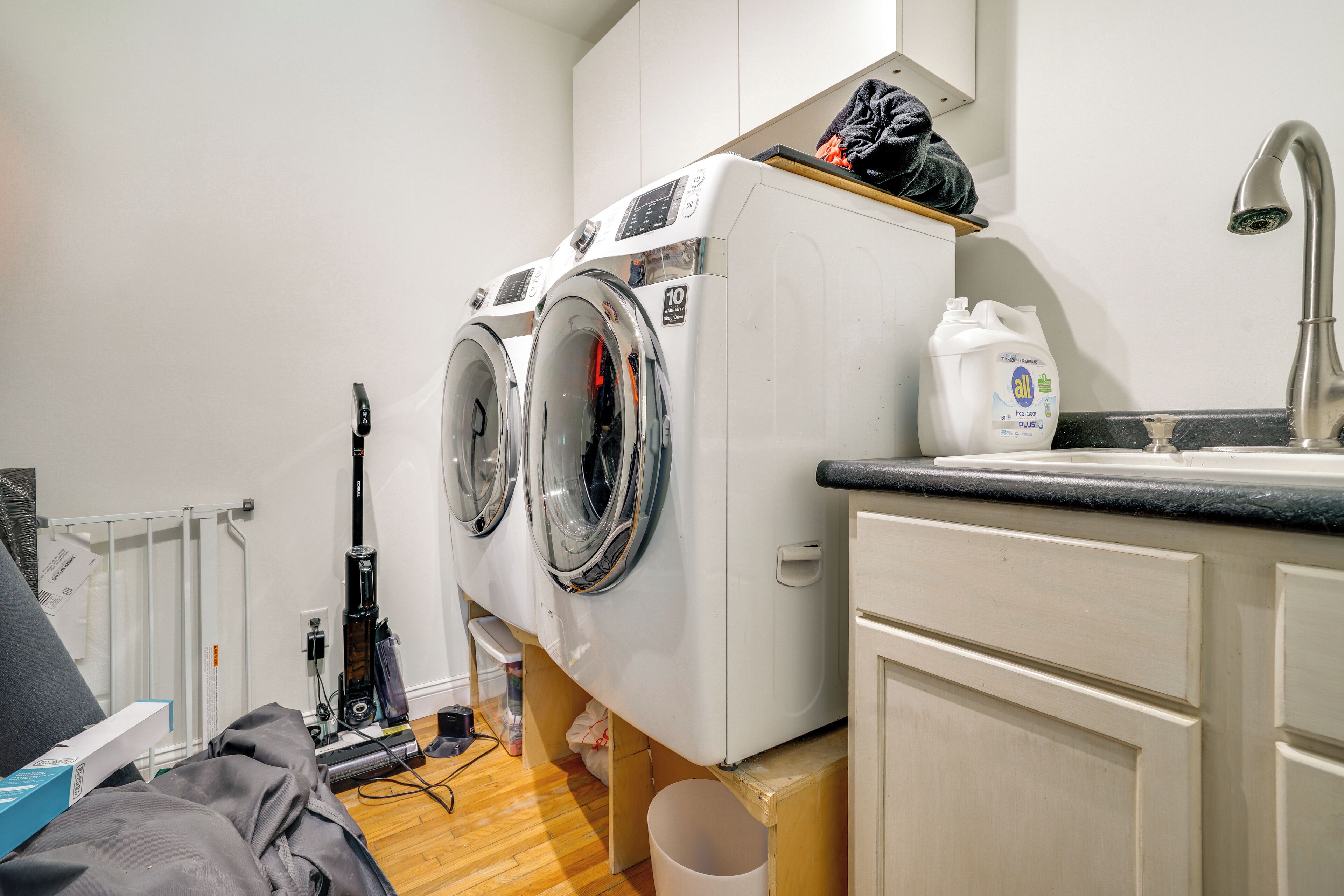 A laundry area with two front-loading washing machines, a sink, and a countertop.