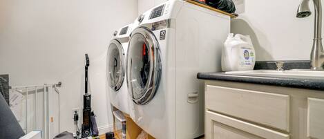 A laundry area with two front-loading washing machines, a sink, and a countertop.