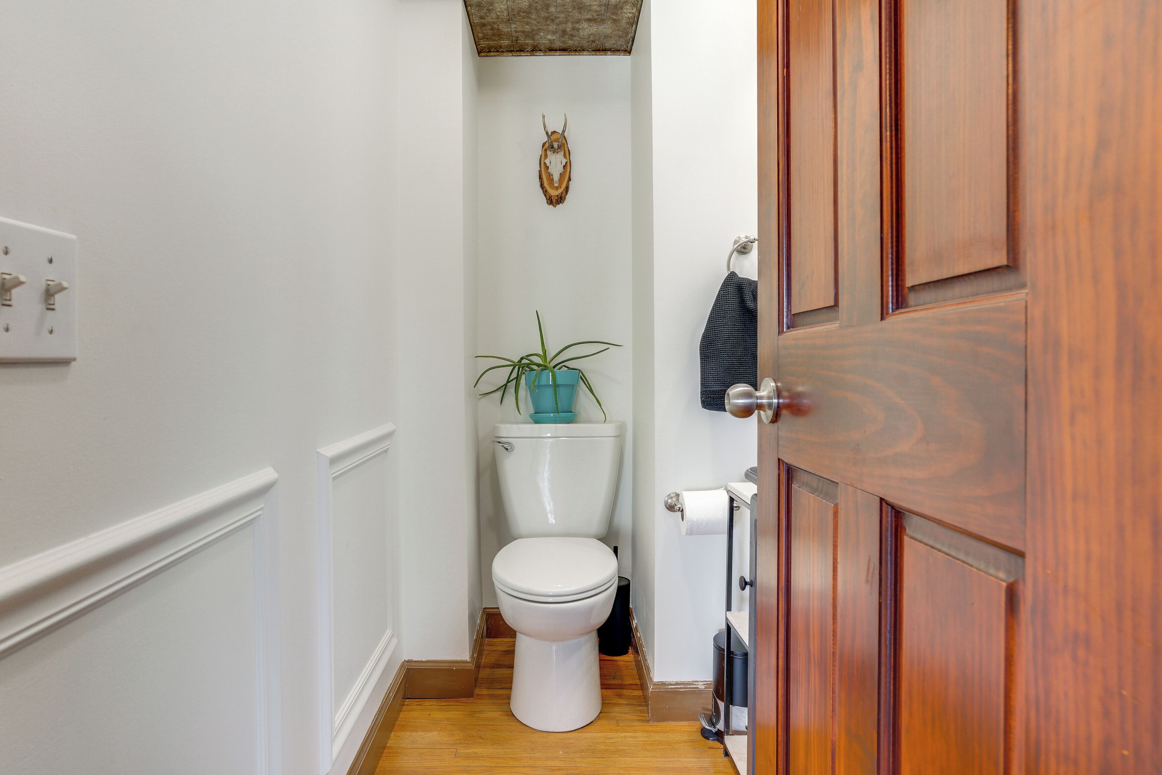 Un bagno piccolo con il water bianco, pavimento in legno, una pianta blu e una porta di legno.