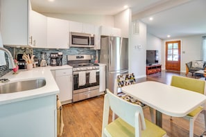 A modern kitchen with stainless steel appliances, a dining area with a white table and chairs, and a living room with a television and seating.