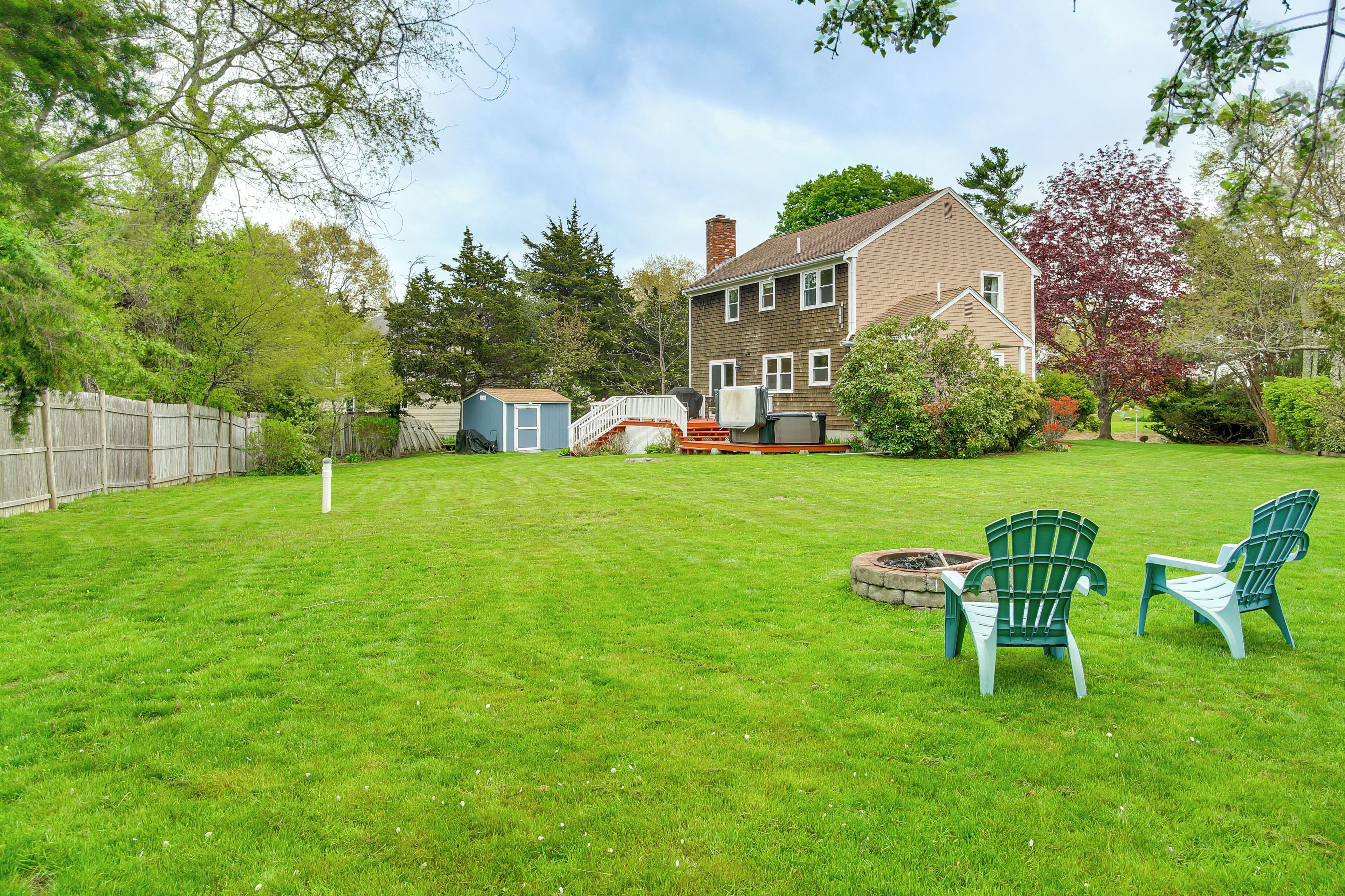 A backyard with a house, a wooden fence, a shed, and two green Adirondack chairs.