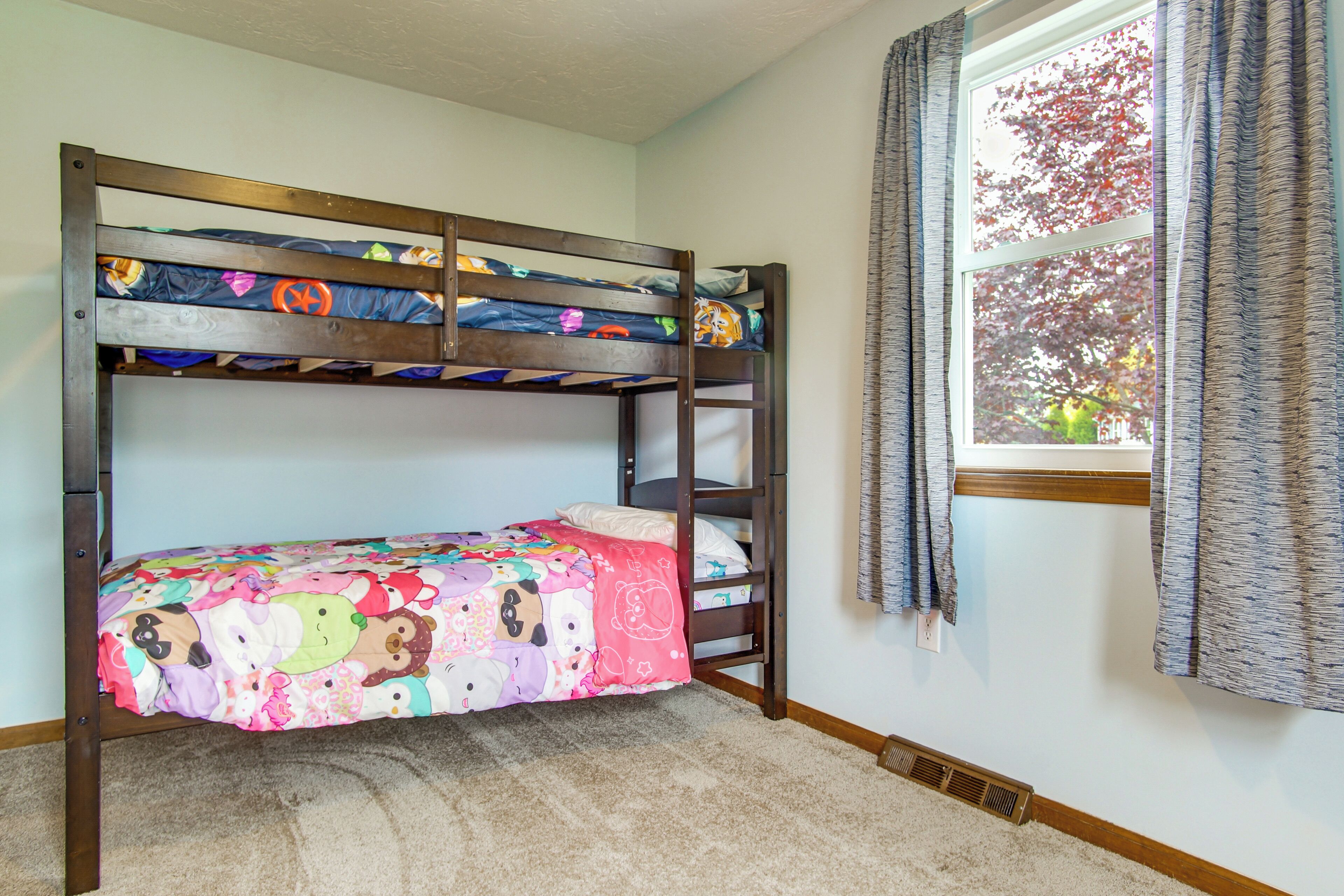 A bunk bed with a colorful bedspread, a window with curtains, and a carpeted floor.