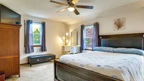 Un dormitorio con cama, ventilador de techo, cómoda, banca y ventana con cortinas.