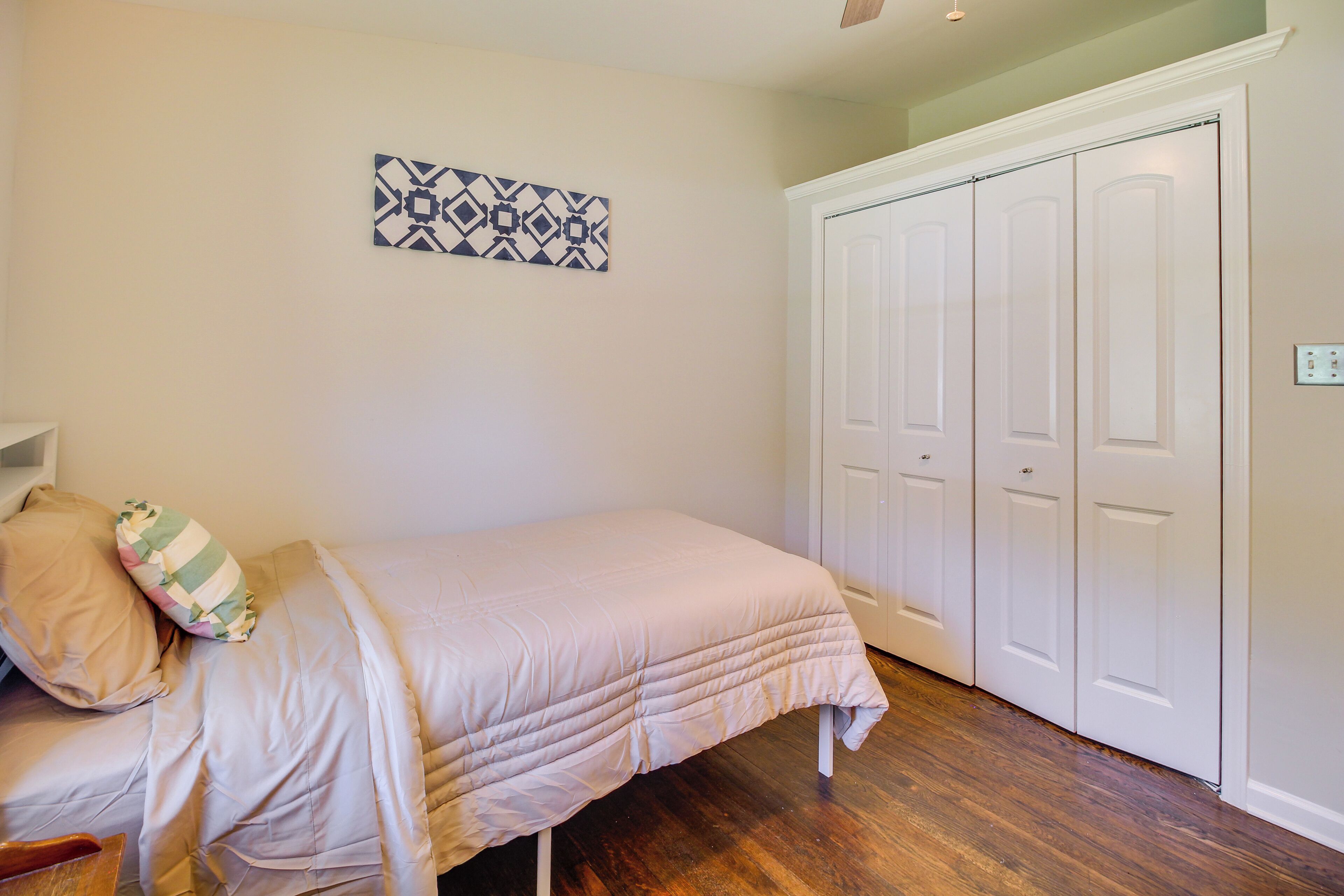A bedroom with a bed, a white wardrobe, and a wall-mounted artwork.