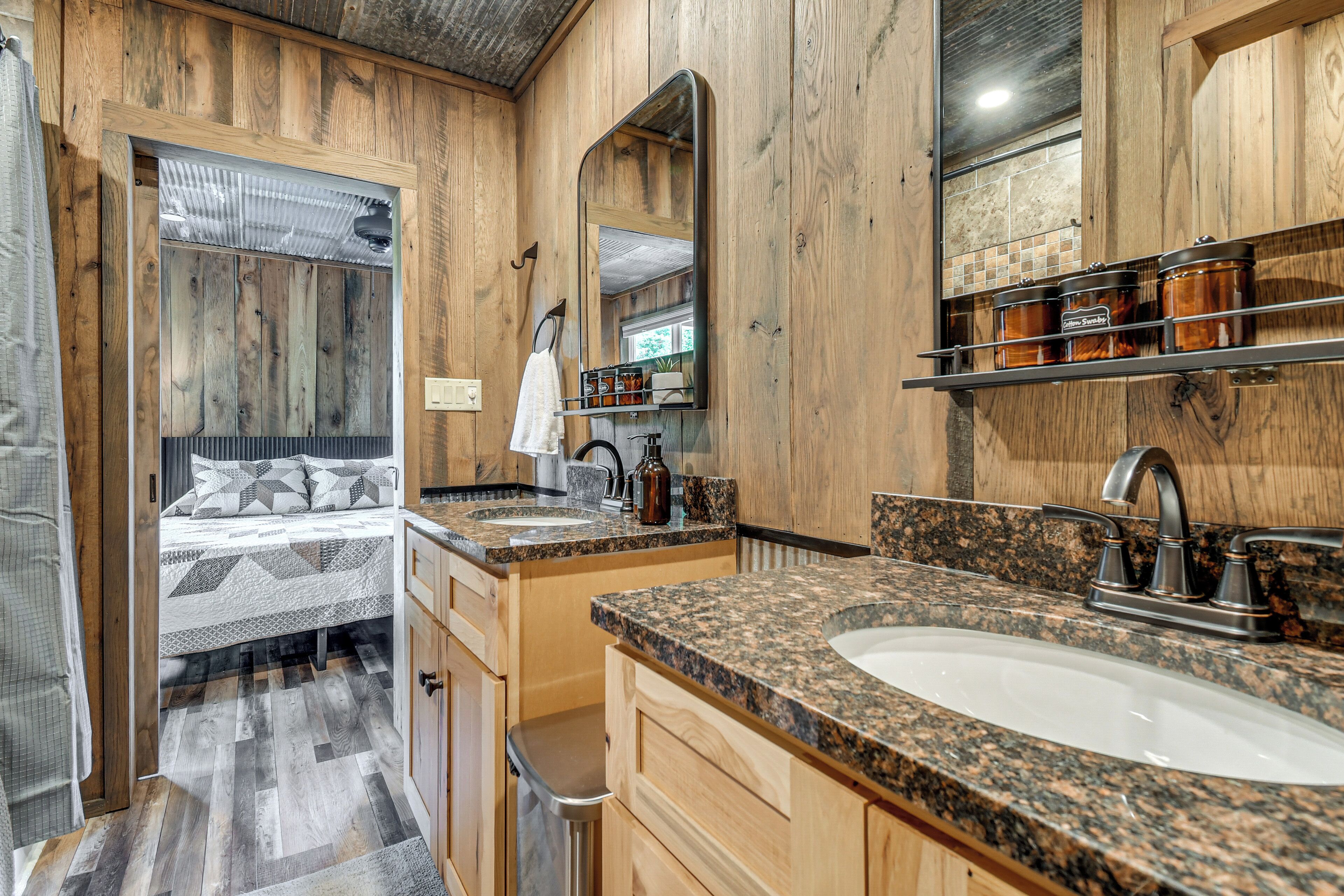 A wooden interior with a bed, two sinks, a mirror, and storage jars.