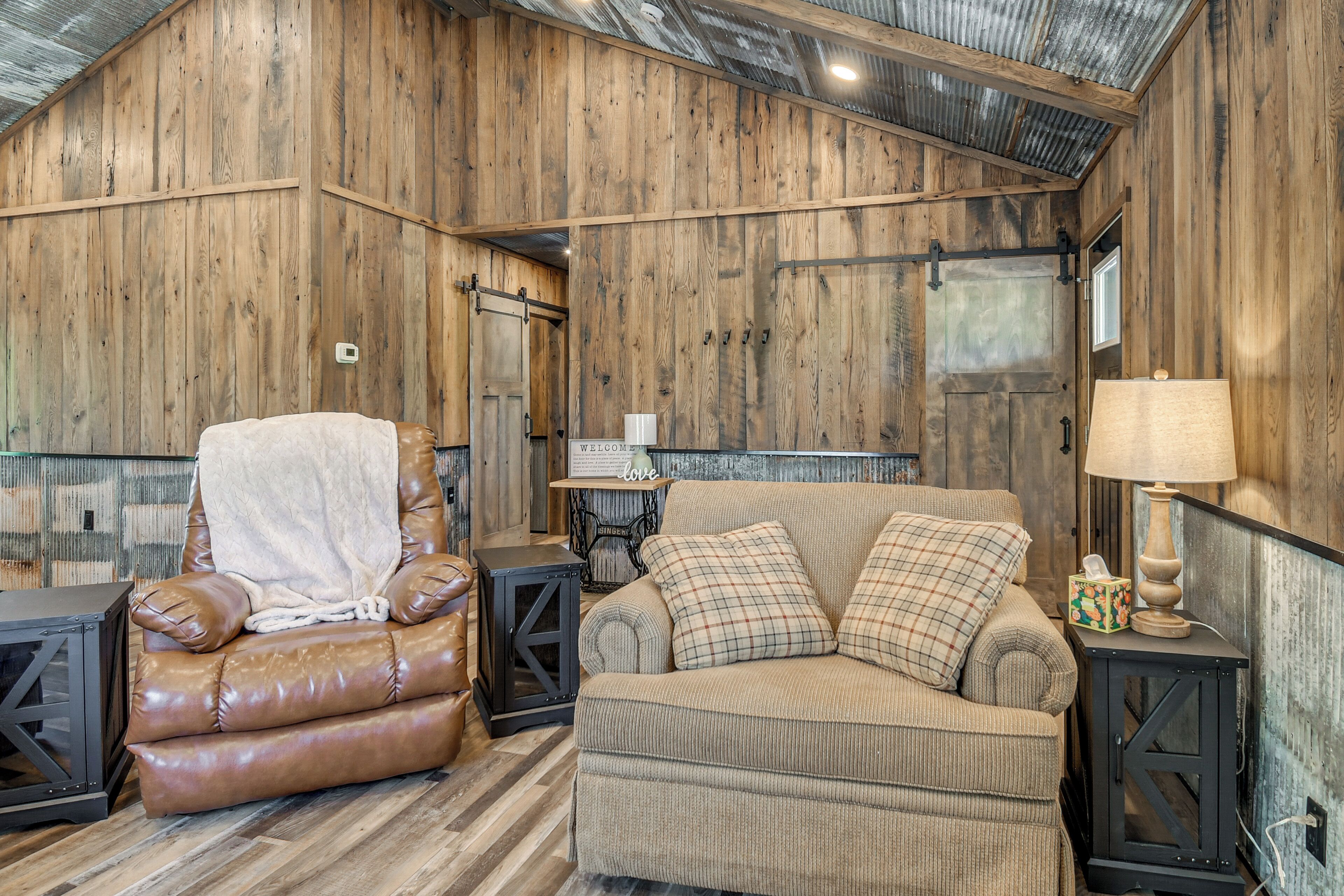 A rustic interior with wooden walls, a leather armchair, a sofa, and a lamp.