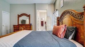 Een slaapkamer met een bed, een kaptafel, een spiegel en een deur naar een andere kamer.