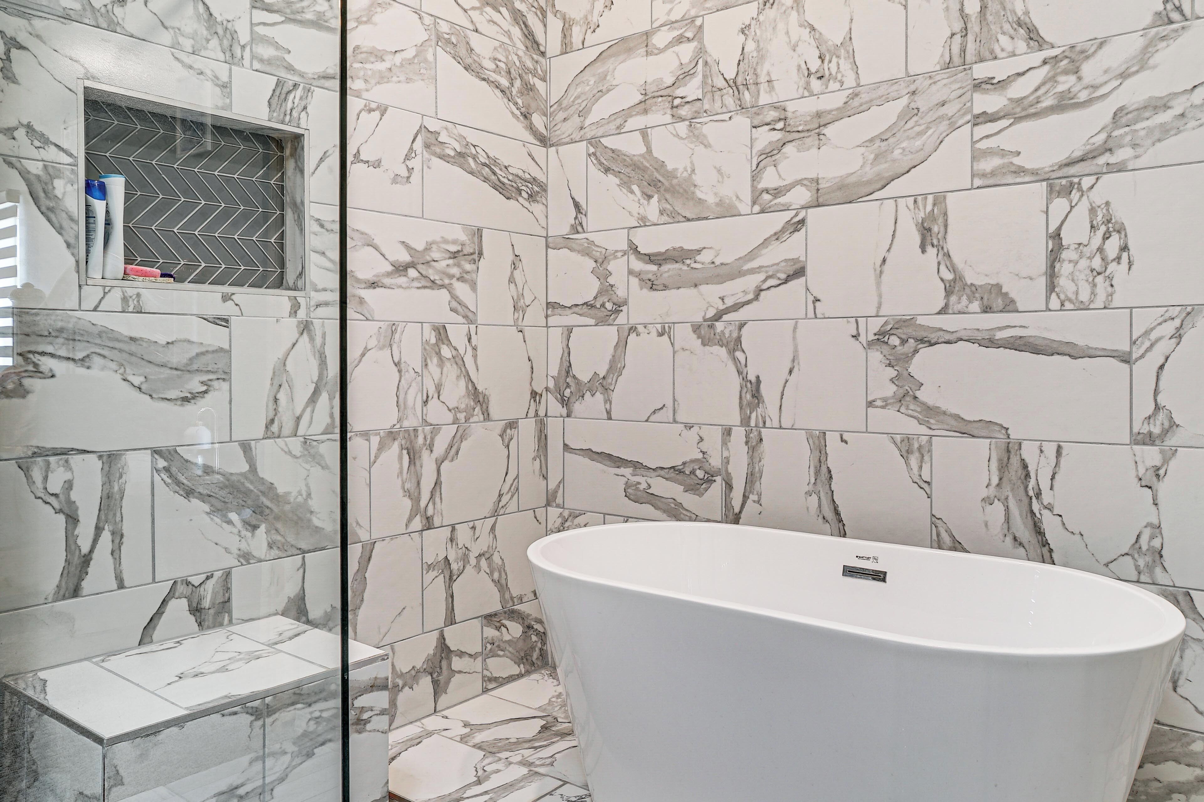 A bathroom with a freestanding bathtub, marble-patterned tiles, and a glass shower enclosure.