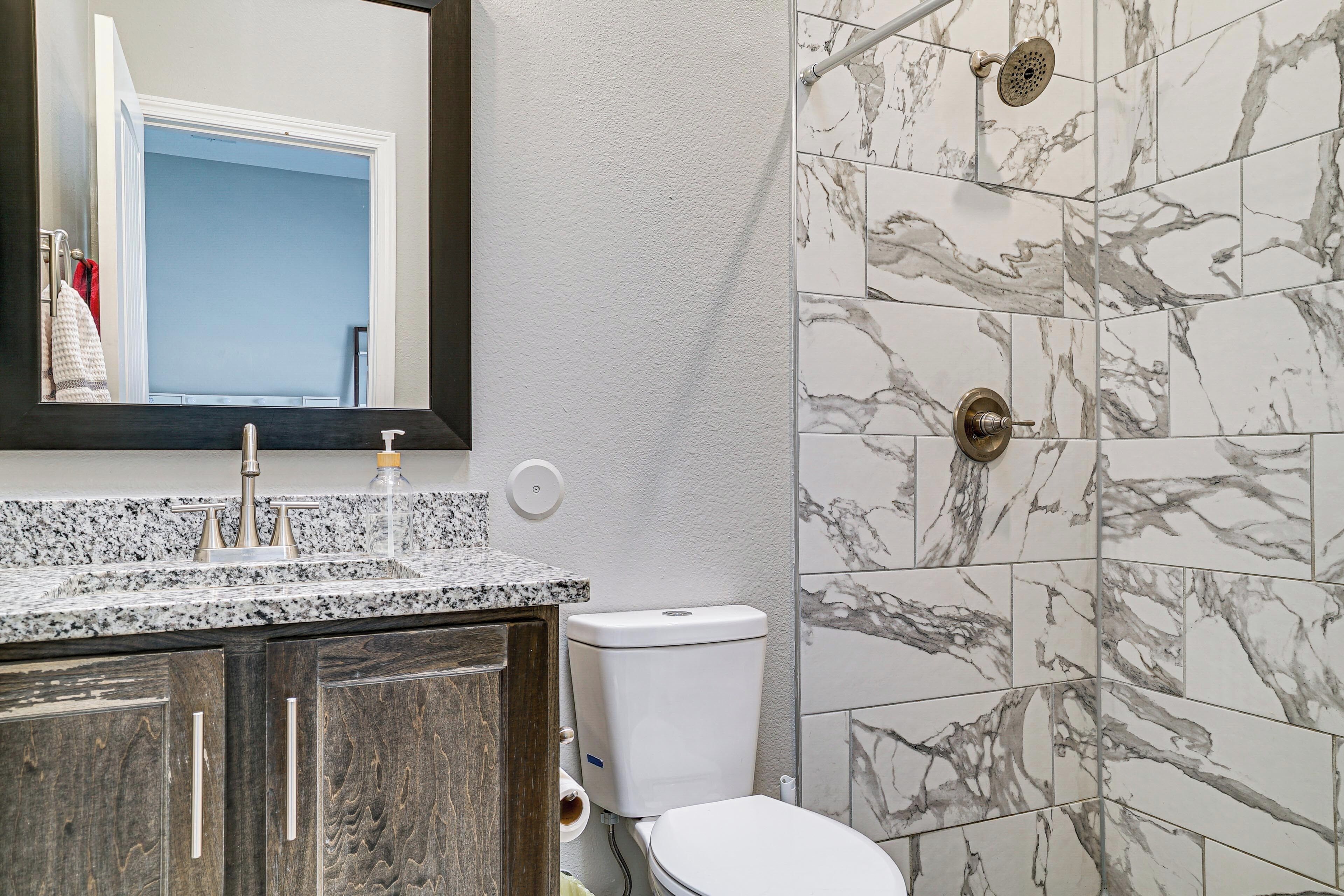 A bathroom with a marble tile shower, a white toilet, a granite countertop sink, and wooden cabinets.