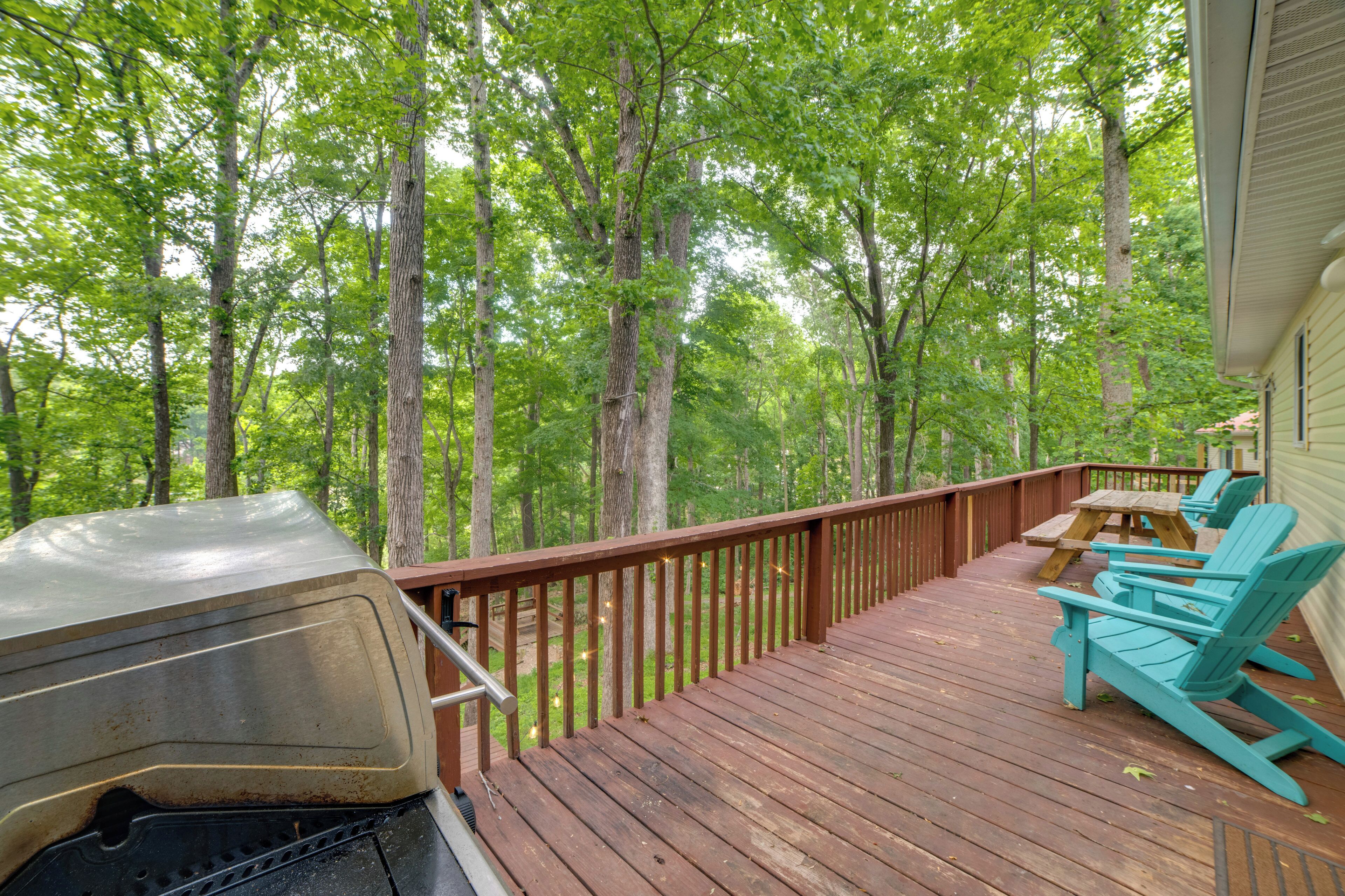 Eine Holzterrasse mit Grill, türkisblauen Adirondack-Stühlen und einem Picknicktisch.