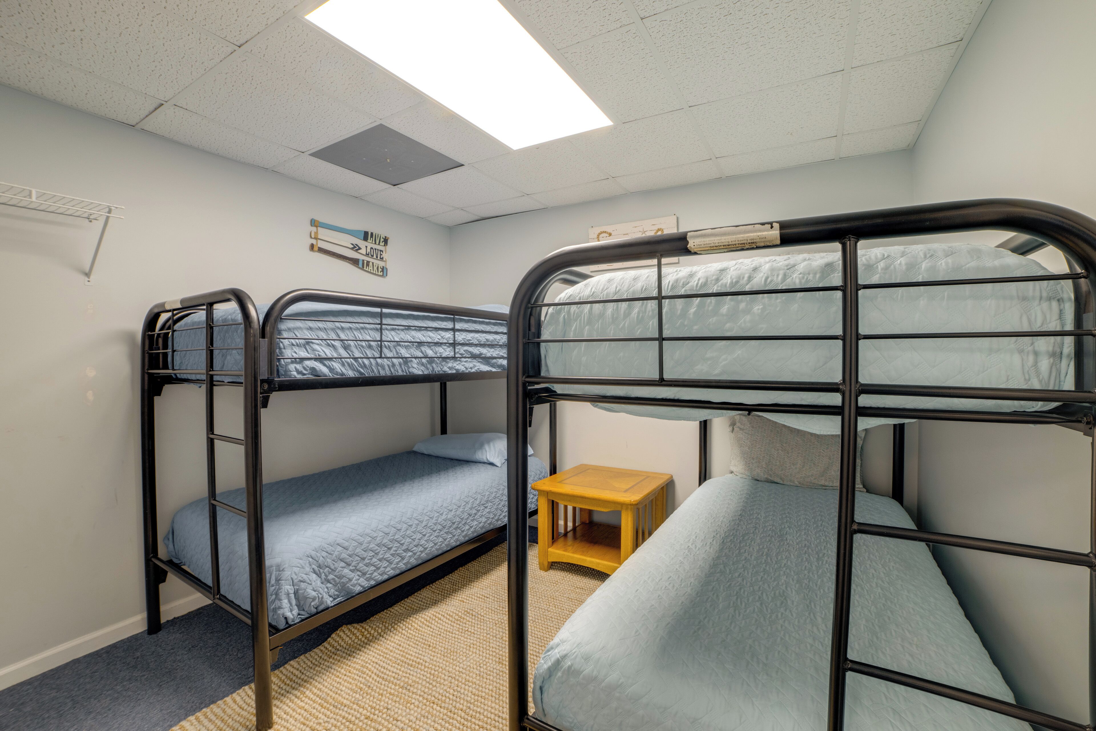 A bunk bed room with a small wooden table, a ceiling light, and a wall-mounted shelf.
