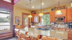 A kitchen with wooden cabinets, a large island with bar stools, pendant lighting, and a stone backsplash. - Dock, Decks & Epic View! Sacheen Lake Family Cabin (Newport)