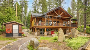 A log cabin with a balcony, stone pathway, and large rocks in the yard. - Dock, Decks & Epic View! Sacheen Lake Family Cabin (Newport)