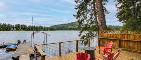 A wooden deck with a view of a lake, red Adirondack chairs, and a small table.