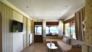 A modern hotel room with a sofa, a small table, and a TV. - Spacious Beachfront Retreat With Large Garden in Ormos Panagias (Sithonia)