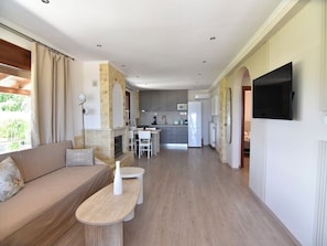 Una sala de estar moderna con un sofá, una mesa de centro y un televisor. Se ve una cocina al fondo.