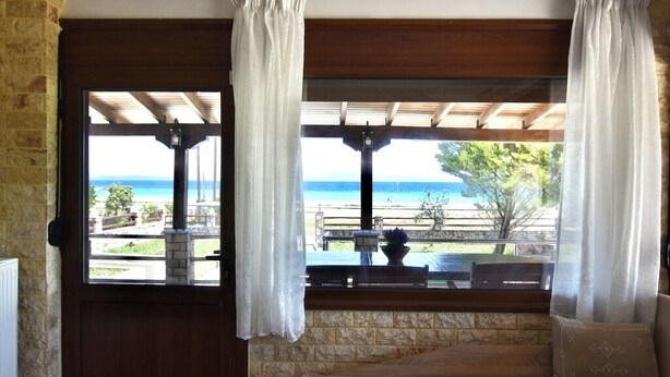 A room with a view of the beach, a wooden door, and a window with curtains. - Spacious Beachfront Retreat With Large Garden in Ormos Panagias (Sithonia)