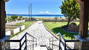 A stone pathway leading to a beach with a clear view of the ocean and a wooden structure with a railing. - Spacious Beachfront Retreat With Large Garden in Ormos Panagias (Sithonia)