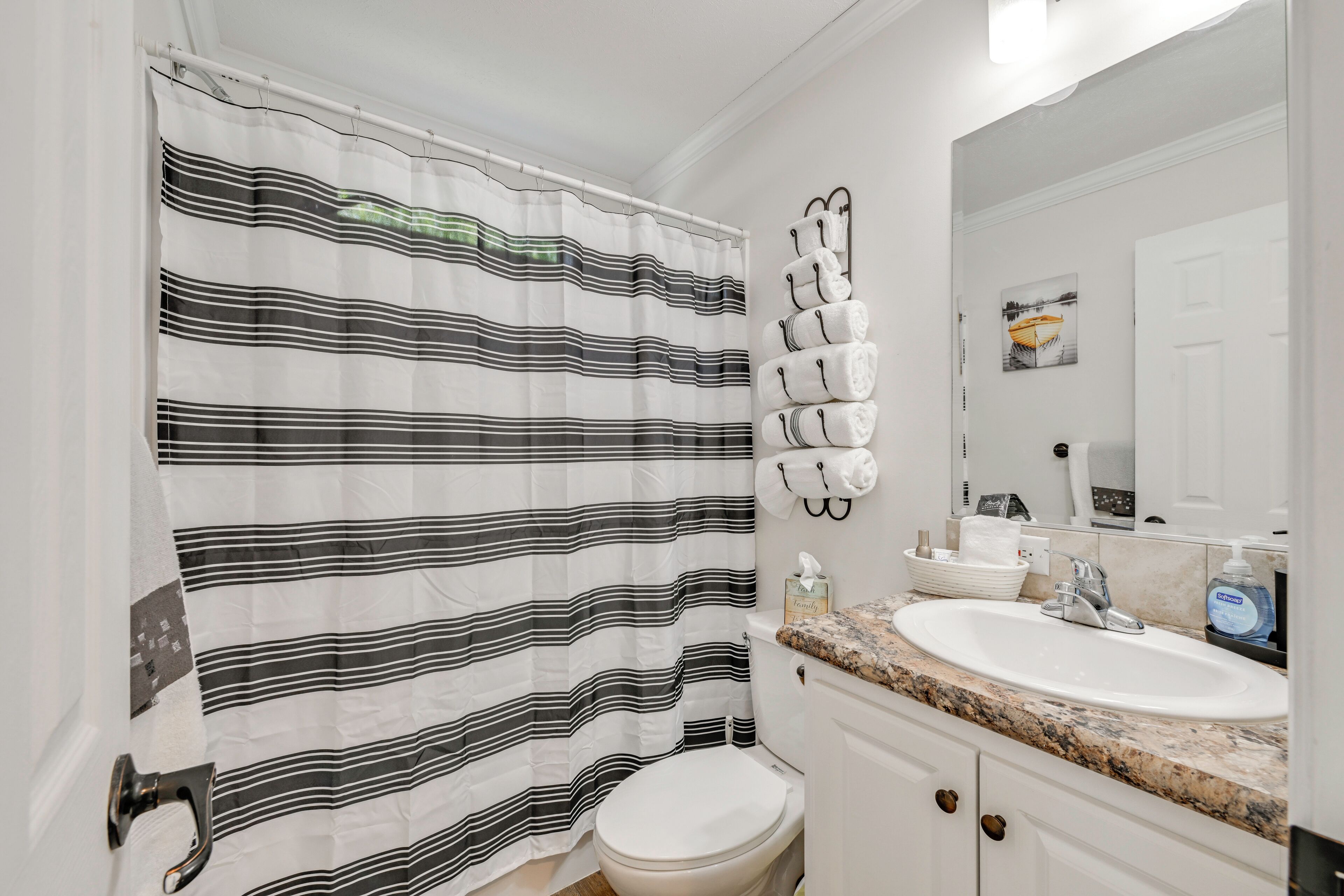 A bathroom with a striped shower curtain, a toilet, a sink with a marble countertop, and a mirror.