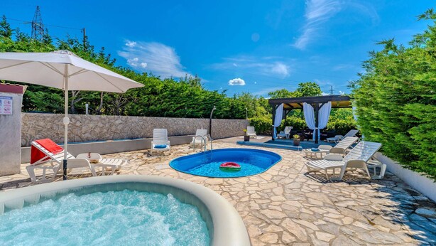 Ein Pool mit Liegestühlen und einer Pergola, umgeben von Steinboden und Grünpflanzen.