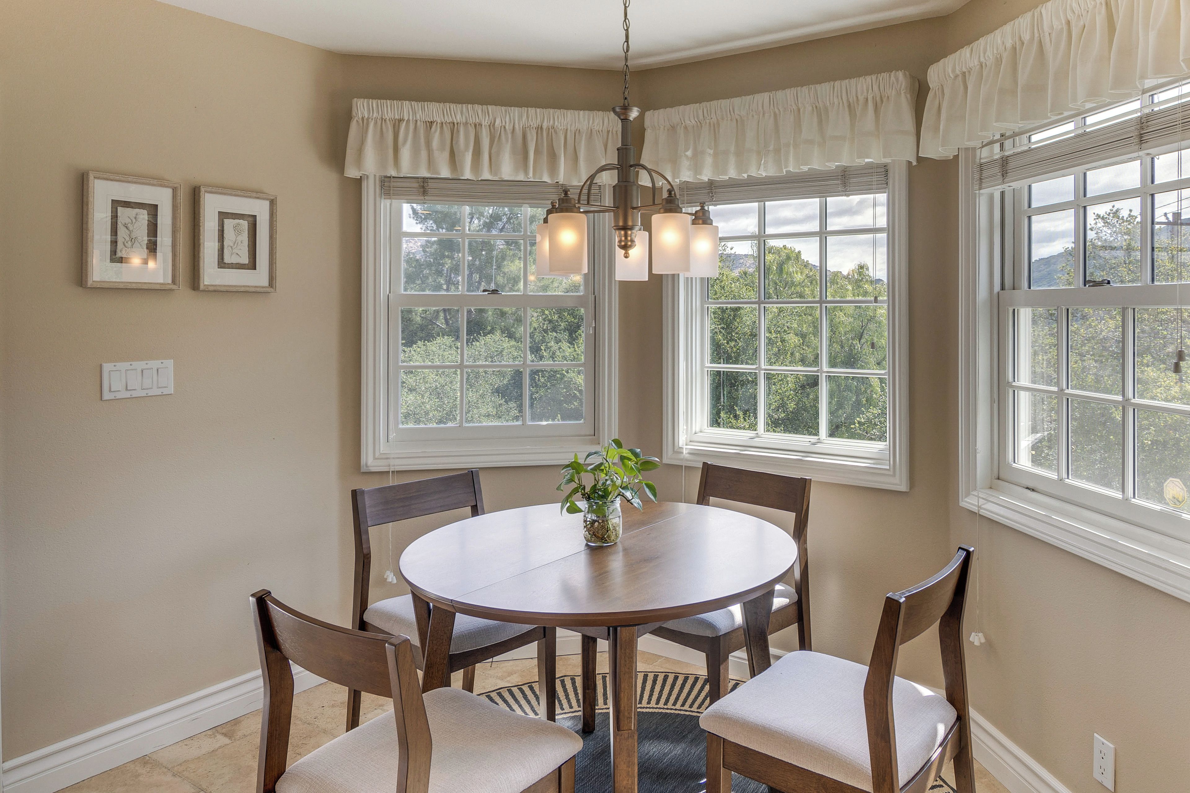 A dining area with a round table, chairs, a chandelier, and large windows with curtains.
