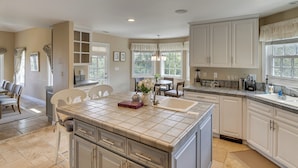 A kitchen with white cabinets, a large island with a sink, and a dining area with chairs and a table. - Combined Retreat w/ Epic Views in Simi Valley! (Simi Valley)