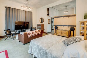 A modern hotel room with a large bed, a sofa, a TV, and a kitchenette.