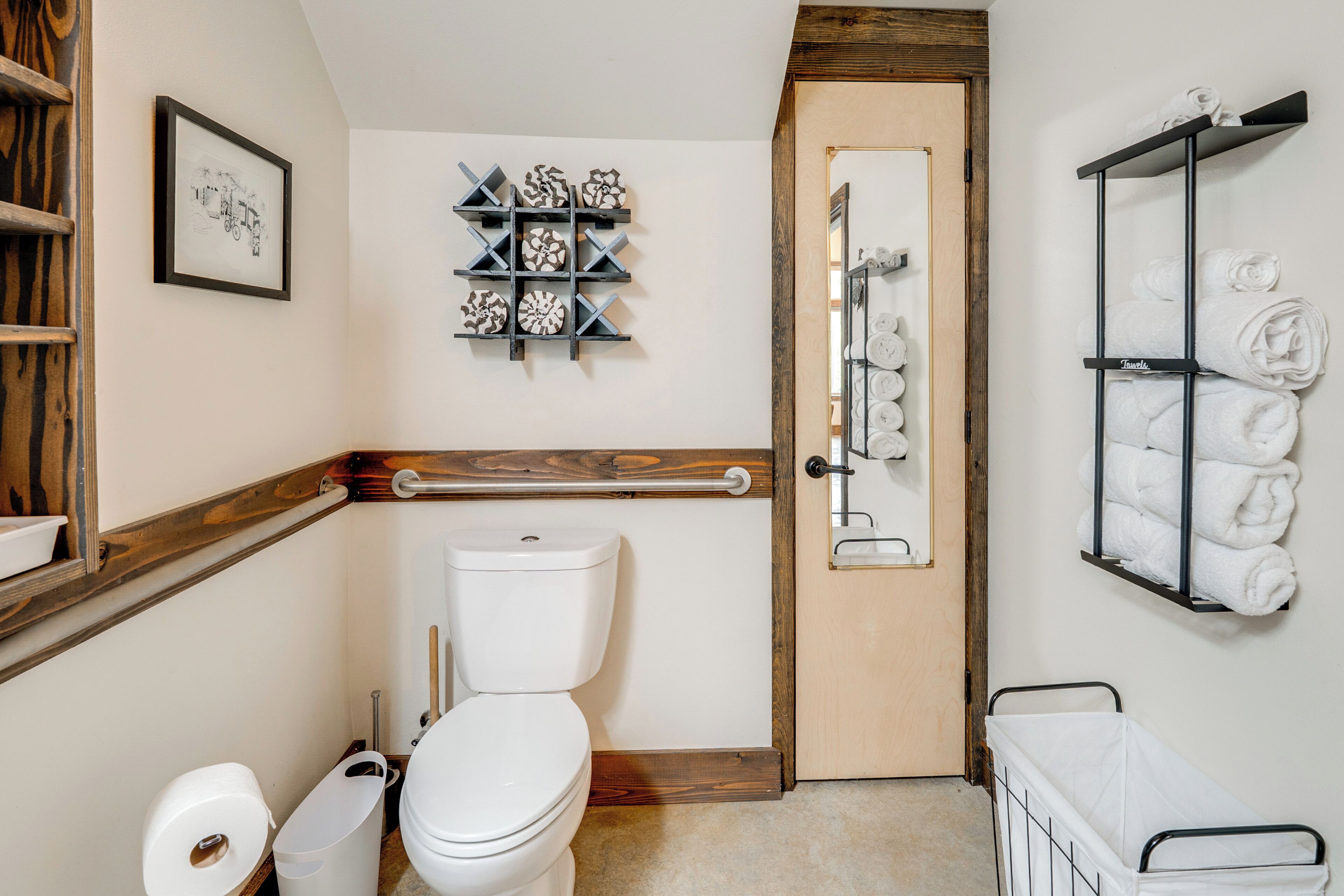 A bathroom with a toilet, a towel rack, a shelf with decorative items, and a wooden door.