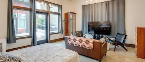 A modern hotel room with a large bed, a sofa, a TV, and a dining area.
