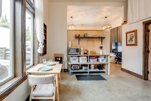 A kitchen with a dining table, chairs, a microwave, and shelves with kitchenware.