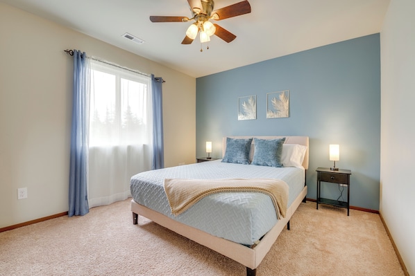Une chambre à coucher avec un lit, un ventilateur de plafond, une table de chevet avec une lampe et une fenêtre avec des rideaux.